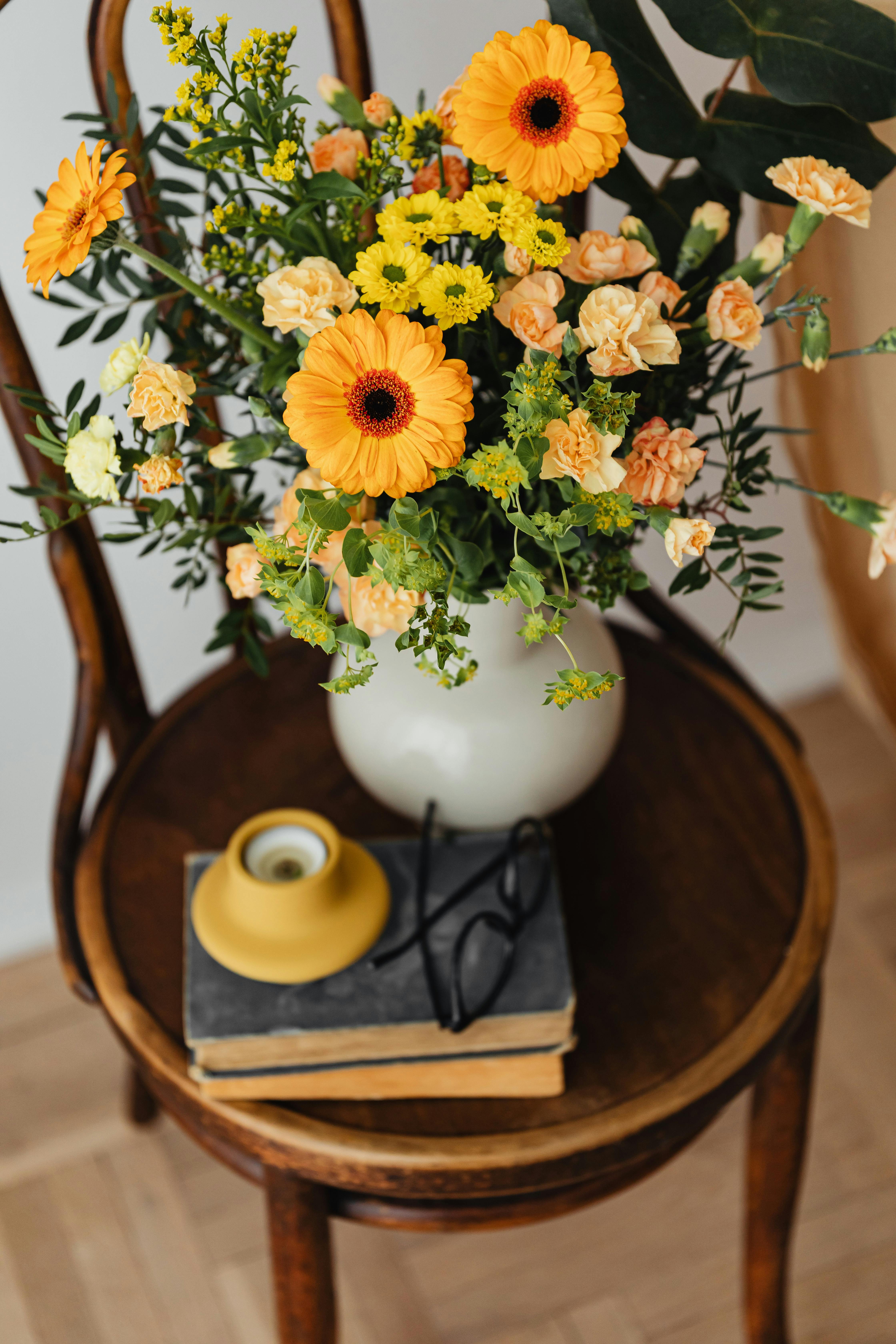 Yellow flowers in a vase on a table, beside glasses and a book.