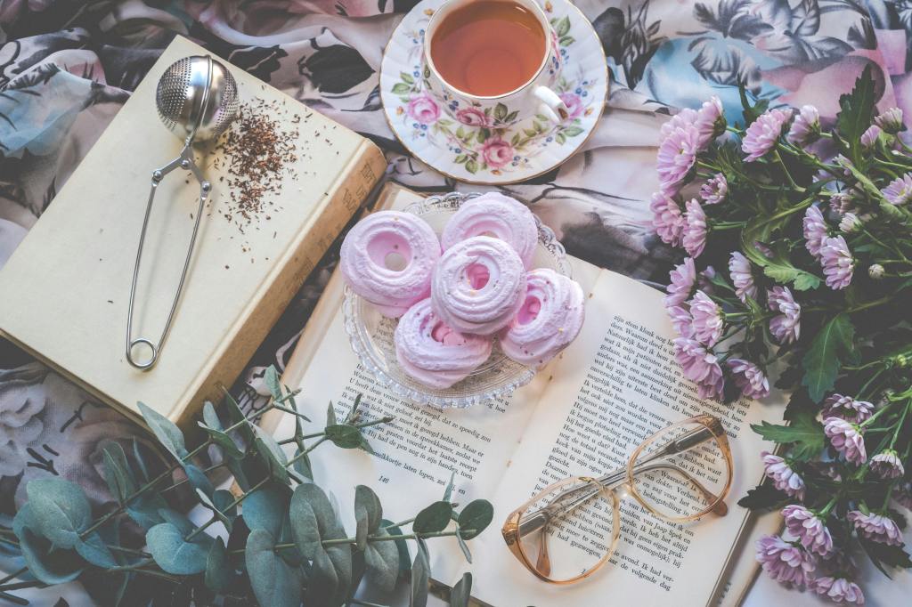 open books with pink flowers spread out around them, antique tea cup, glasses