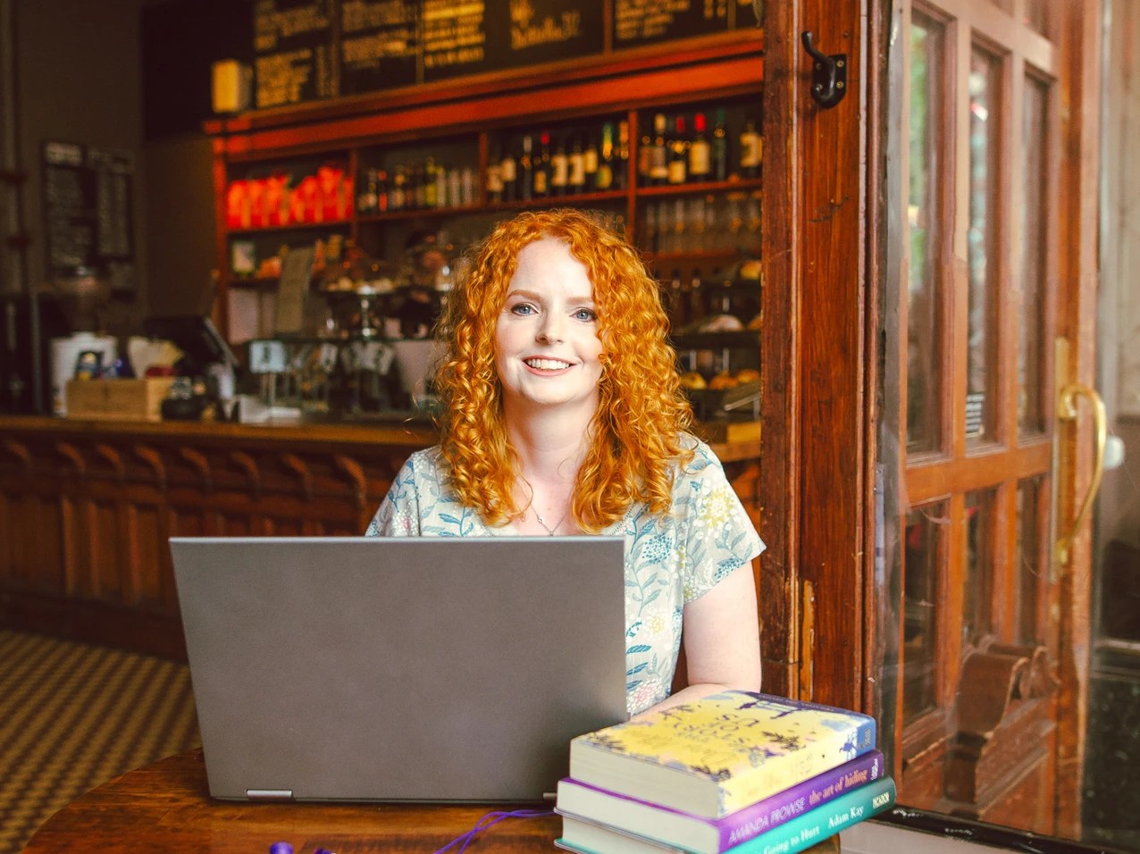 red-headed woman in a cafe with books, laptop