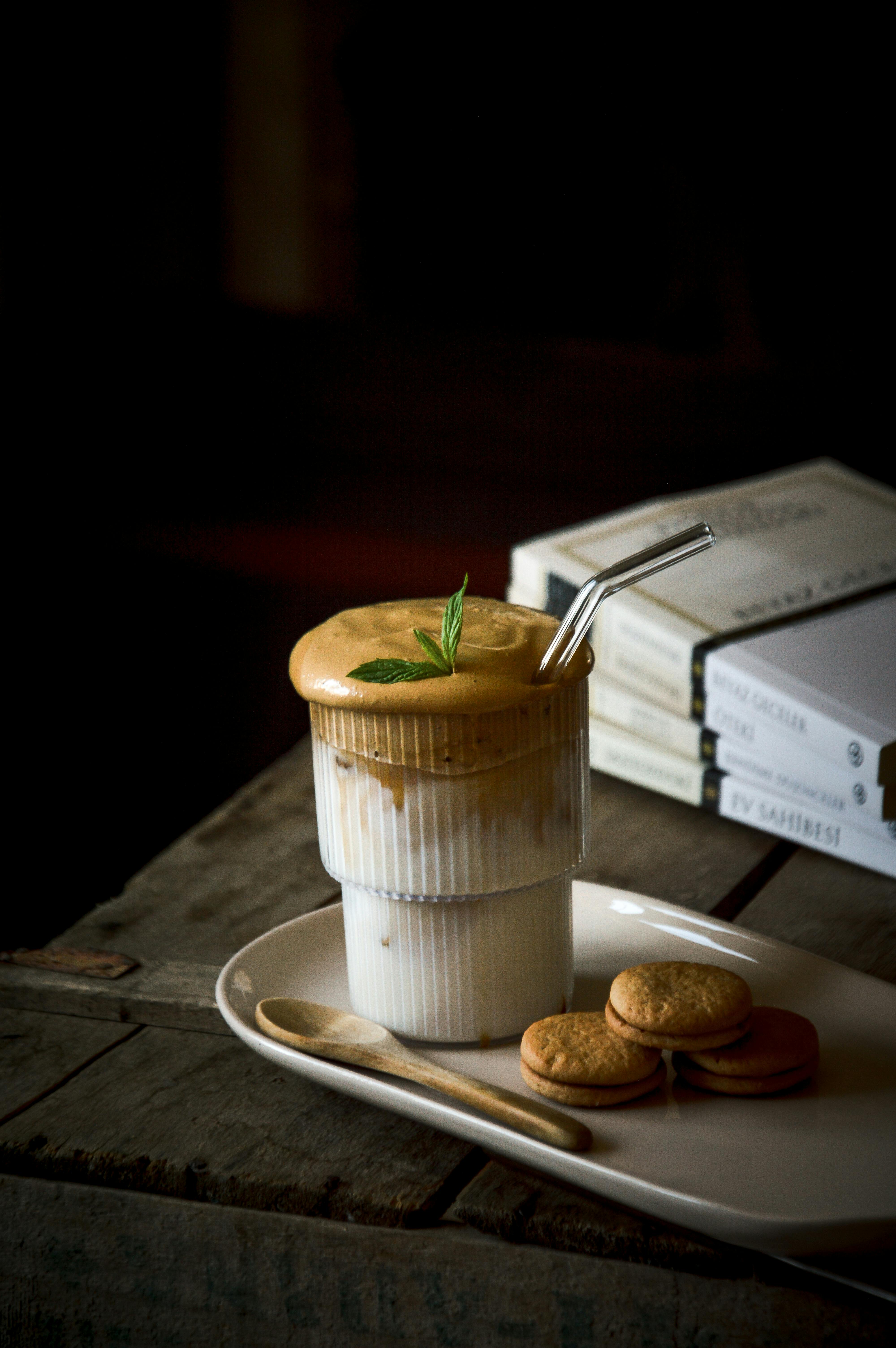 Overflowing coffee in a glass with a straw, book stack, some dessert that's slightly in frame.
